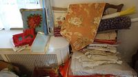 Wide view showing assorted linens including folded towels, napkins, table runner or fabric pieces, and pillows on a shelf by a window