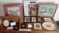 Photo showing various pictures and frames arranged on a wooden surface including larger framed prints, small frames, and decorative tray.