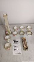 Full lot arranged on a marble surface showing eight small salt pots, two little salt spoons with holder, and tall decorative vase.