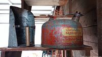 Side view of vintage metal gasoline can and metal seed scooper on wooden shelf, showing label and surface wear