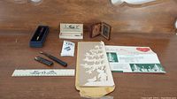 Full overview of vintage lot with items arranged on table including paper Christmas decoration cutout, wooden ruler, letter opener, small cutter in case, wood-like picture frame