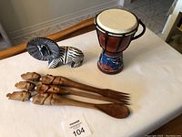Wide shot showing soapstone lion, small drum, and set of wooden utensils on white table
