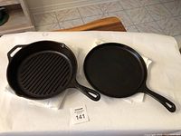 Two Lodge cast iron skillets, one grill skillet with ridges and one flat skillet, placed side by side on white cloth.