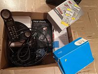 Box with Clarity Professional C4220 cordless phone handset, adapter, cables, and unopened packs of hearing aid batteries including Siemens brand, stacked items with packaging and instruction manual visible.