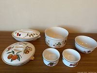 Angle showing all seven pieces: 9 inch oval and 8 inch round vegetable servers with lids, four bowls including two small soufflé dishes and one Wedgwood soufflé dish