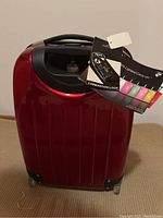 Front angled view of red Heys XCase carry-on luggage with combination lock tags hanging from handle.