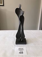 Front view of the black steel sculpture "Mentor" by Kramer showing two abstract figures on a rectangular base.