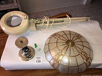 Full view of magnifying lamp on adjustable arm and capiz shell ceiling light fixture on table with electrical cord coiled