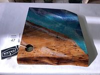 Top view of handcrafted ocean board showing blue epoxy ocean waves and ambrosia maple wood grain with live edge and hole near edge.