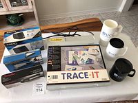 Overview of entire lot on table showing all items including light box, staplers, pencil sharpener, tracing paper pad, and plastic mugs.