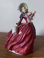 Full view of the Royal Doulton Autumn Breezes figurine in a red flowing dress holding a dotted basket.