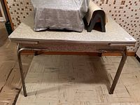 Front-facing photo of retro laminate and chrome kitchen table, showing top surface and tubular chrome legs, with some wear visible on legs.
