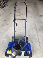 Front view of the blue SnowJoe electric snow blower showing the handle, wheels, and chute.