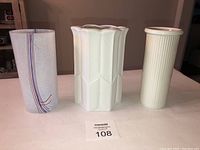 Three vases displayed side-by-side on a plain surface with a lot number card, showing sizes and design details.