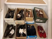 Eight pairs of women's shoes and slippers arranged in their original boxes on stairs. Shoes include leather flats, slippers, and slingbacks mostly in darker colors. Boxes show brand labels including Antonietta.
