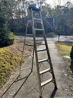 Full view of an 8-foot tall aluminum step ladder standing outdoors on a driveway, showing the ladder fully opened and ready for use.