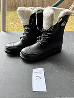 Side view of a pair of black waterproof winter boots with white fleece lining and Michael Kors logo emblem on the side. Black laces with Michael Kors branding.