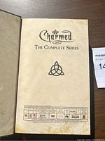 Opened DVD set showing Charmed The Complete Series title page with triquetra symbol.
