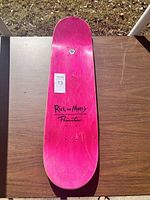 Photo showing top side of pink skateboard deck with Primitive and Rick and Morty logos