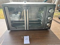 Front view of silver Oster countertop oven showing double glass doors, two silver door handles, and control panel on right side.