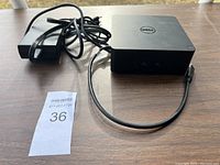 Front and connected power adapter view of the Dell docking station on a wooden surface with Masold tag.