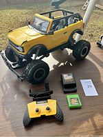 Full side and front angled view of the large yellow RC Bronco with included charger, battery, and remote on a wooden table.