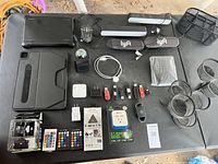 Top view of electronic and office equipment laid out on a black table including tablets, earbuds, USB flash drives, chargers, LED light bars, and accessories.
