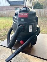 Front side view of Shop-Vac unit with hose attached showing brand and red power switch.