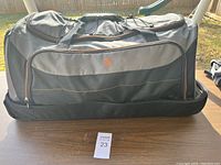 Front view of large black travel bag with logo and orange trim placed on table outside.