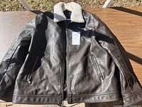 Dark brown leather jacket with front zipper and side zippered pockets laid flat on table, showing full front.