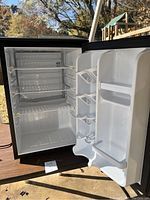 Open mini fridge showing interior with three wire shelves and freezer compartment.