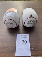 The pair of white Bluetooth speakers with decorative grille and rose gold accents shown front-facing on a wooden surface.