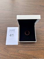 Ring in white open box with black velvet interior, showing black exterior with faint red edges.