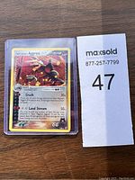 Front of Team Magma's Aggron Pokémon card in protective sleeve with auction lot number next to it.