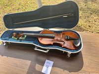 Full view of violin with bow inside open hard case on table outdoors.