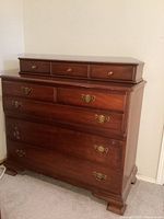 Front-side angle view shows the entire dresser, the eight drawers, wood finish, brass pulls, and the bracket feet design.