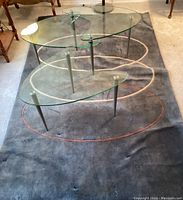 Top view of two glass artist palette-shaped tables nested on wool area rug showing chrome legs and abstract rings on rug