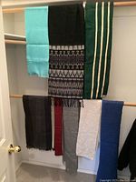 Nine scarves displayed hanging, showing different colors and patterns including solid, stripes, and geometric designs.