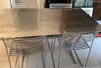 Dining table and four metal chairs shown from various angles illustrating the brushed metal textured table top, metal chair design with horizontal slats, and table leg construction.