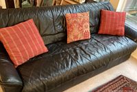 Front view of black faux leather couch with three throw pillows