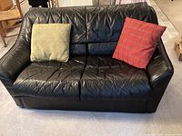 Front view of black faux leather love seat with green and red throw pillows.