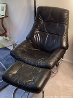 Front angle of black faux leather Stressless chair and ottoman showing chrome bases