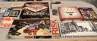 Overview photo showing the collection of board games and card games spread on table including Scrabble, Risk, Red Letter, Port Townsendopoly, Domino set, and multiple card decks.