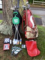Red Spalding leather golf bag, black Quiver bag, green Sport Seat, assorted golf balls, gloves and accessories on grass near tree