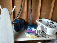 Photo showing Kenmore vacuum in blue with hose, ironing board, iron, hamper and vacuum bags on table