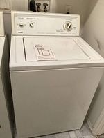 Overall front view of the Kenmore top load washing machine with manual on lid.