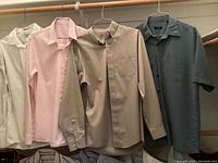 Eight men's dress shirts hanging on hangers, including solid colors and striped patterns, in a closet setting.