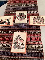 Overall display of four signed Northwest Pacific Indigenous prints laid out on a patterned textile, with a painted stone egg and frog tile in the center.