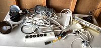 Photo showing multiple items on a table including black spotlight lamp, metal dome lamp, multiple power strips, and electrical cords.