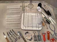 Overview of kitchen supplies including dish rack, utensils, knives, and openers arranged on countertop.